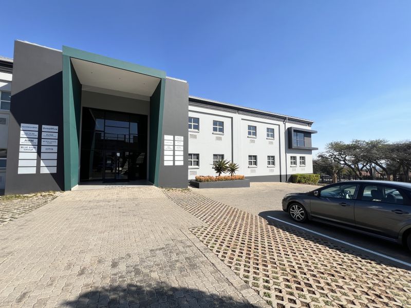 Modern office building exterior featuring a prominent glass entrance, paved parking area, and professional multi-tenant signage.