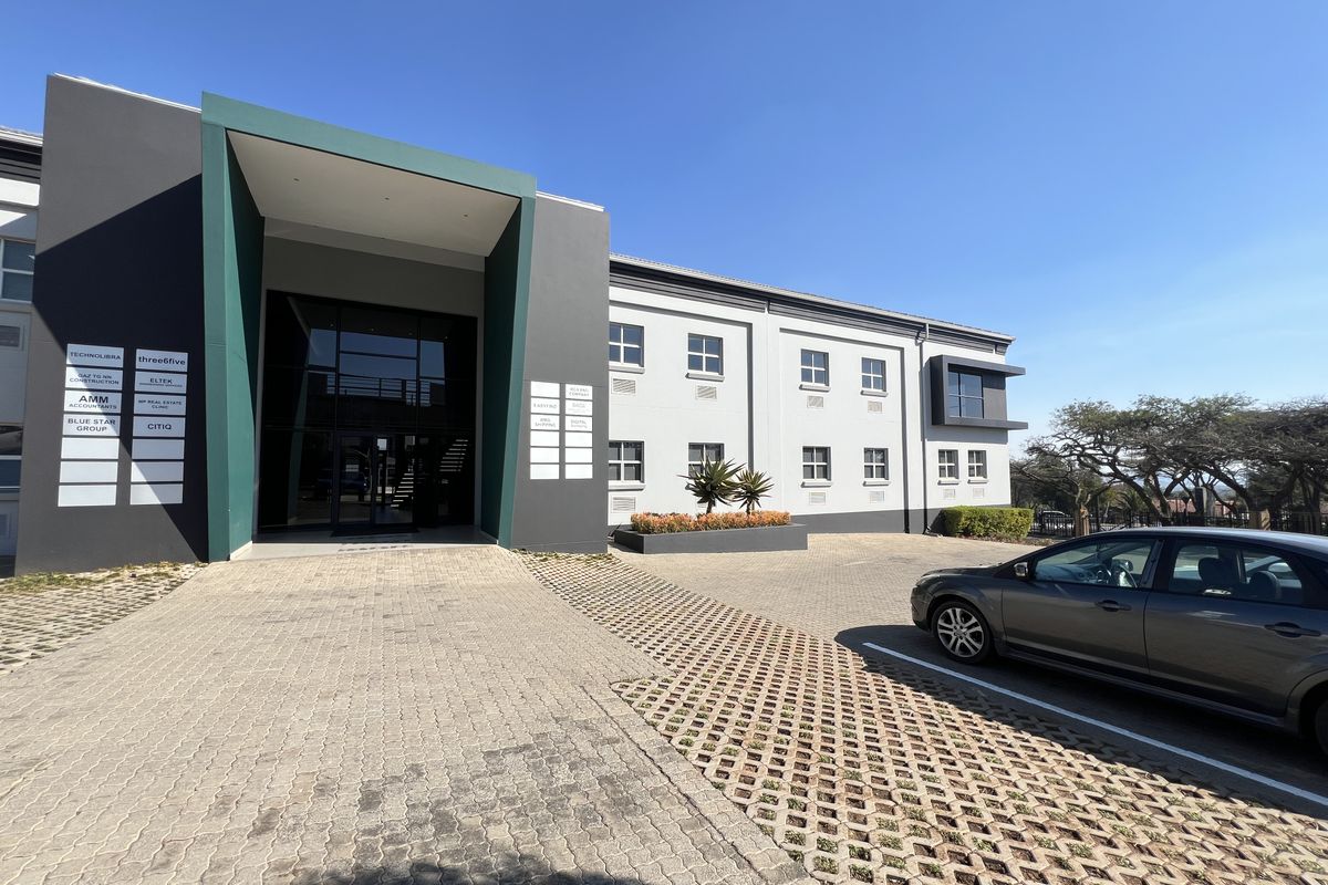 Modern office building exterior featuring a prominent glass entrance, paved parking area, and professional multi-tenant signage.