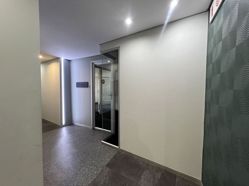 Modern office hallway featuring terrazzo flooring, recessed downlighting, linear LED accent lighting, and a glass-paneled door.