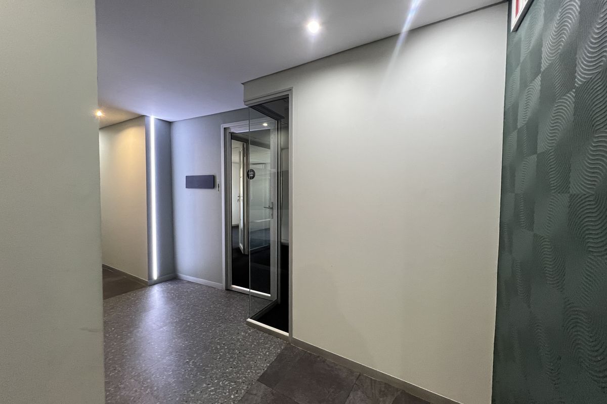 Modern office hallway featuring terrazzo flooring, recessed downlighting, linear LED accent lighting, and a glass-paneled door.