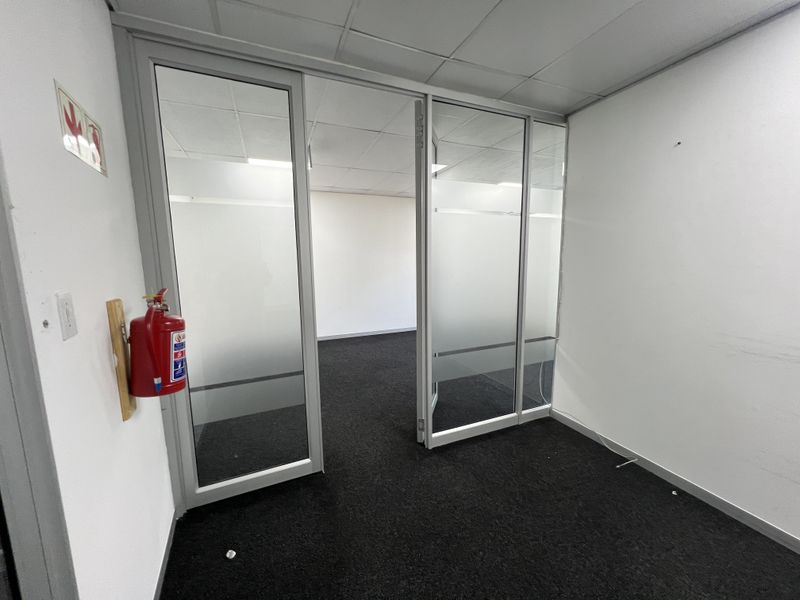 An empty office space featuring a glass partition, suspended ceiling, and dark carpet flooring, suitable for a professional workspace.