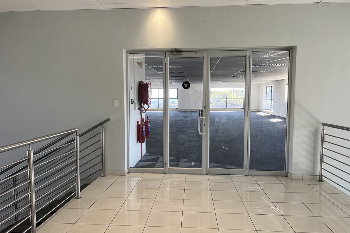 A bright, vacant office suite entrance featuring glass doors, tiled flooring, and integrated fire safety equipment, ready for professional fit-out.