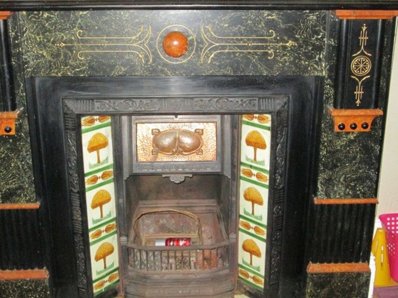 A detailed view of an ornate, vintage-style fireplace mantel featuring decorative ceramic tiles and a cast iron insert.