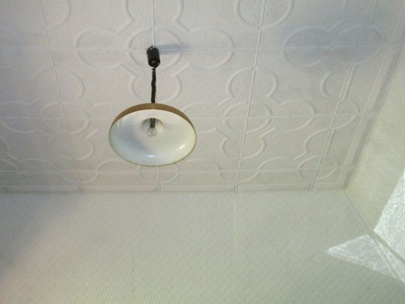 A close-up view of a white pressed metal ceiling with a simple pendant light fixture.