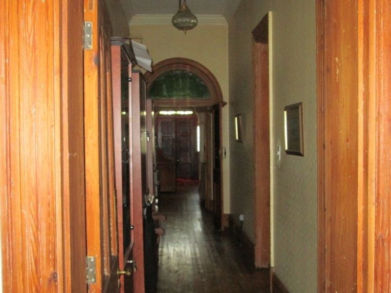 A narrow interior hallway featuring traditional timber door frames, an arched entryway, and original timber flooring in need of cosmetic refurbishment.
