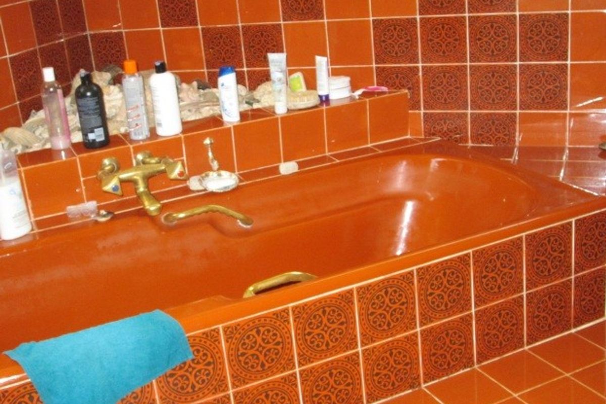 A dated bathroom featuring a built-in bathtub with brass fixtures and distinctive orange decorative ceramic wall and surround tiling.