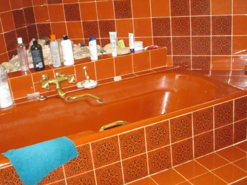 A dated bathroom featuring a built-in bathtub with brass fixtures and distinctive orange decorative ceramic wall and surround tiling.