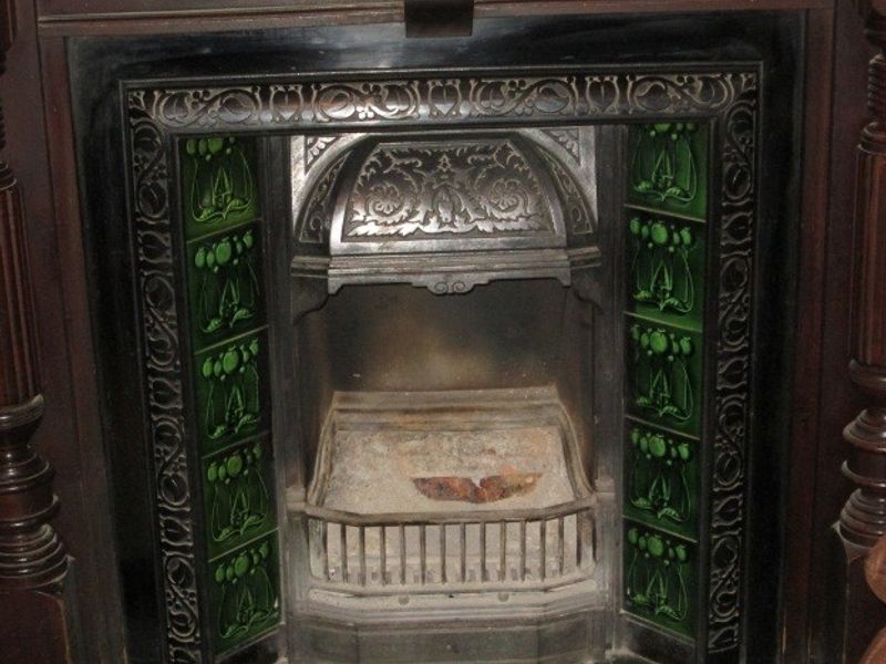 A detailed view of a traditional cast iron fireplace featuring ornate metalwork and decorative green ceramic side tiles.