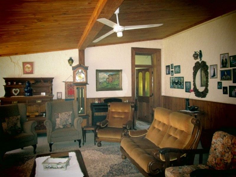 A rustic living room featuring a timber-clad ceiling with exposed beams, ceiling fan, and timber wainscoting, showing signs of wear and wall cracking.
