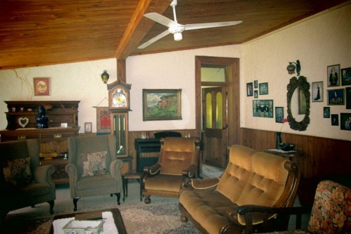 A rustic living room featuring a timber-clad ceiling with exposed beams, ceiling fan, and timber wainscoting, showing signs of wear and wall cracking.