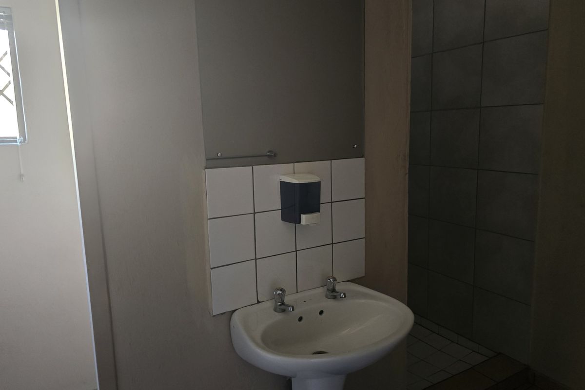 A functional bathroom featuring a pedestal basin with a tiled splashback and a separate tiled shower enclosure.