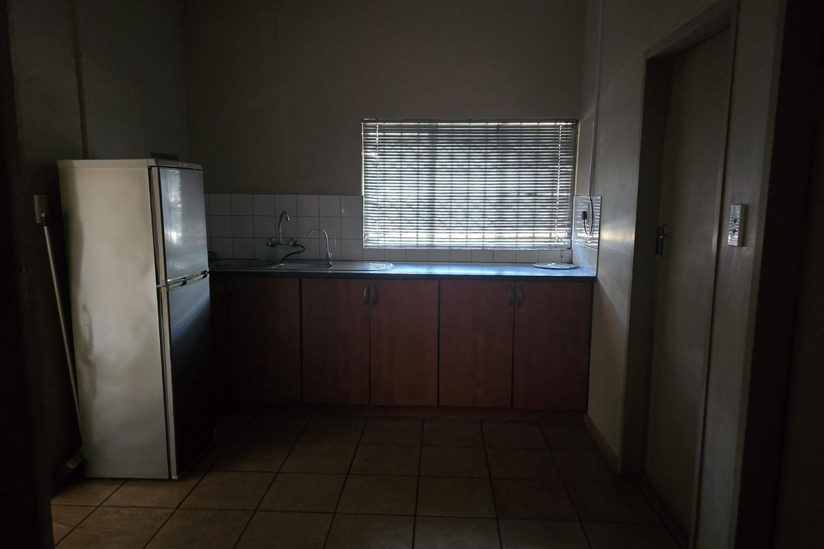 A functional kitchen area featuring tiled flooring, built-in cabinetry, a stainless steel sink, and a tiled splashback, currently requiring improved lighting.