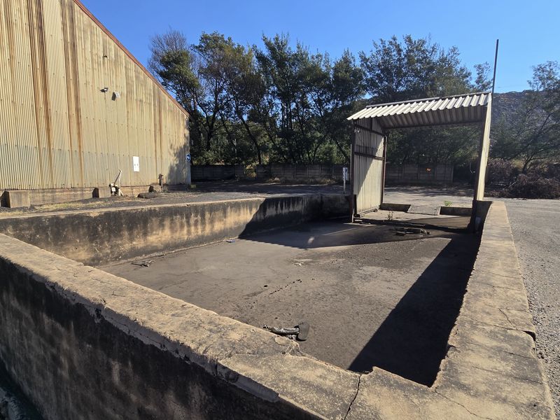 Industrial exterior area featuring a concrete loading bay, corrugated metal building facade, and a metal canopy structure in a weathered condition.