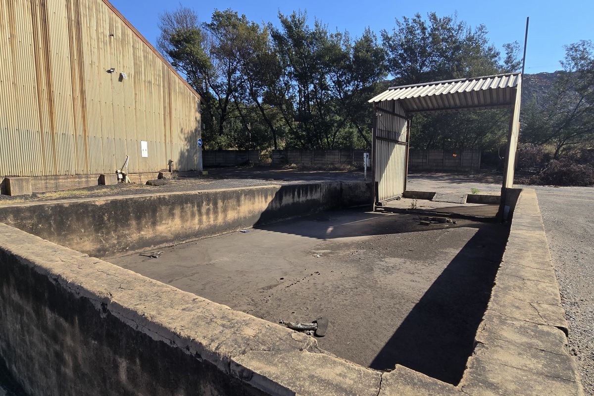 Industrial exterior area featuring a concrete loading bay, corrugated metal building facade, and a metal canopy structure in a weathered condition.