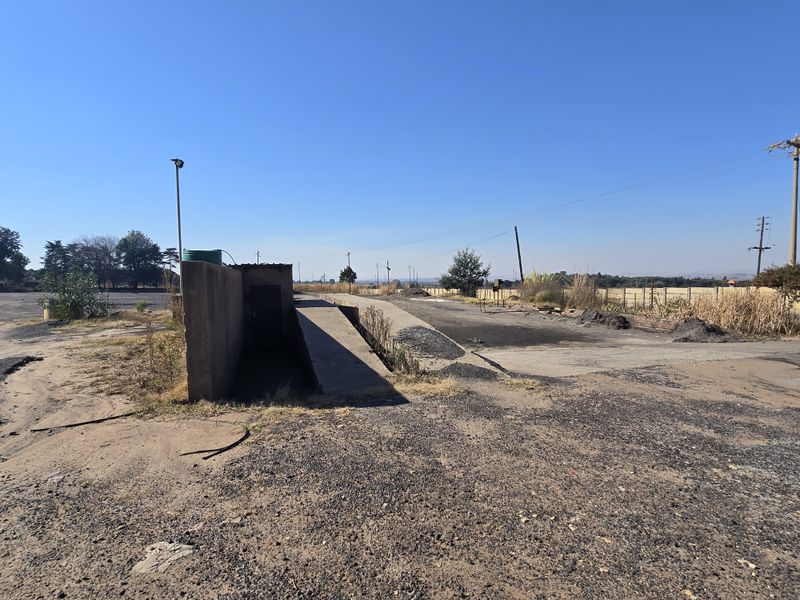 Industrial yard area featuring a concrete loading ramp, asphalt surfacing, and perimeter fencing, suitable for heavy vehicle access and logistics operations.