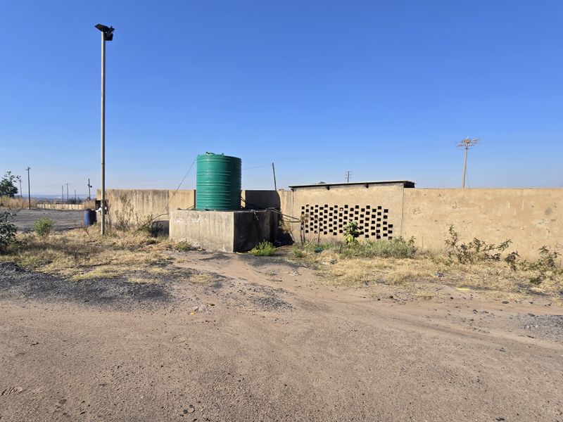 Exterior rear area featuring a water storage tank on a concrete plinth, perimeter wall with ventilation bricks, and a security floodlight.