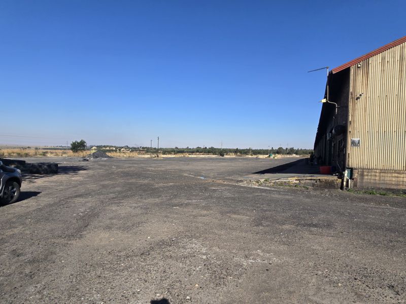 Expansive industrial yard area featuring a large warehouse structure with corrugated metal cladding and a paved asphalt surface.