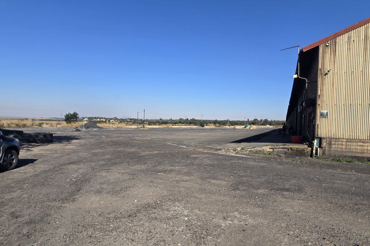 Expansive industrial yard area featuring a large warehouse structure with corrugated metal cladding and a paved asphalt surface.