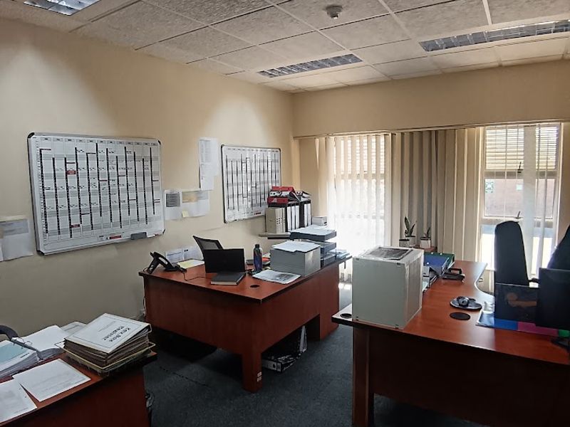 A functional office space featuring a suspended ceiling with recessed lighting, carpeted flooring, and vertical blinds providing natural light.
