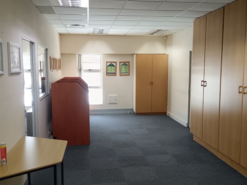 A functional office space featuring a suspended ceiling with recessed lighting, carpeted flooring, and ample built-in storage cabinetry.