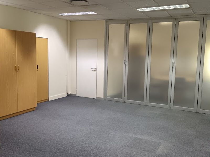 An empty office space featuring a suspended ceiling, recessed lighting, built-in storage cabinetry, and frosted glass partition doors.