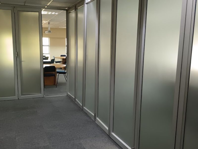A professional office hallway featuring frosted glass partitions, aluminum framing, carpeted flooring, and a suspended ceiling with recessed lighting.