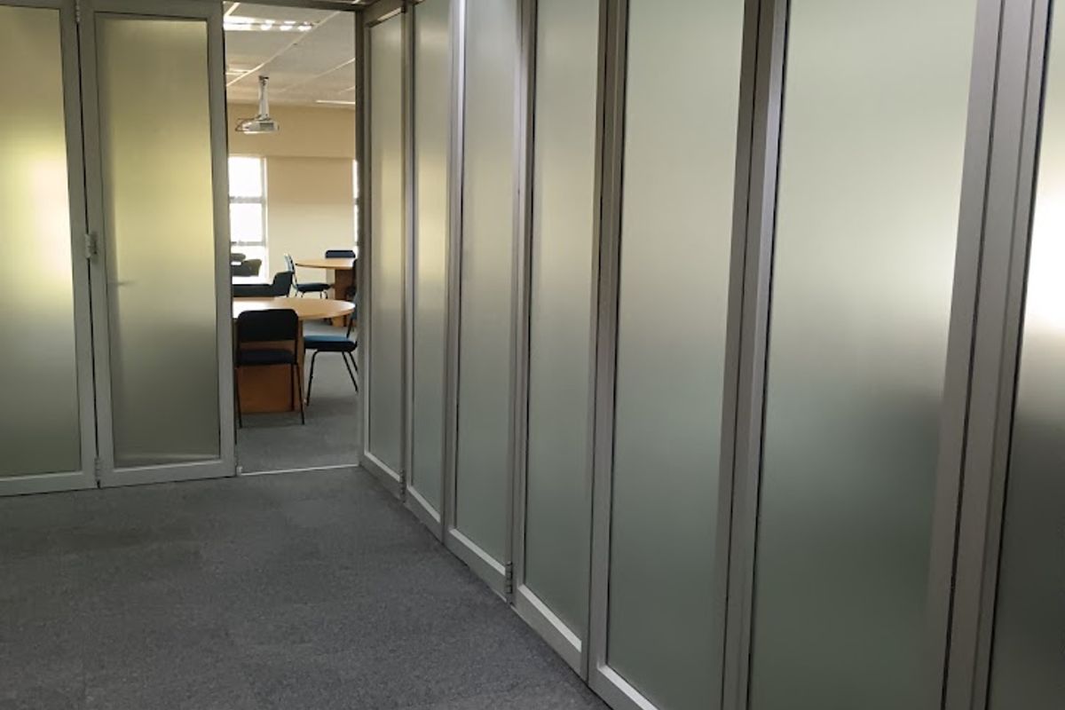 A professional office hallway featuring frosted glass partitions, aluminum framing, carpeted flooring, and a suspended ceiling with recessed lighting.