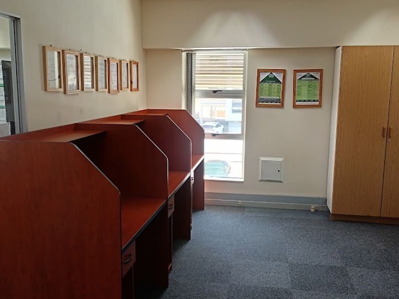 A functional office space featuring built-in wooden workstations, integrated storage cabinetry, carpeted flooring, and a suspended ceiling with recessed lighting.