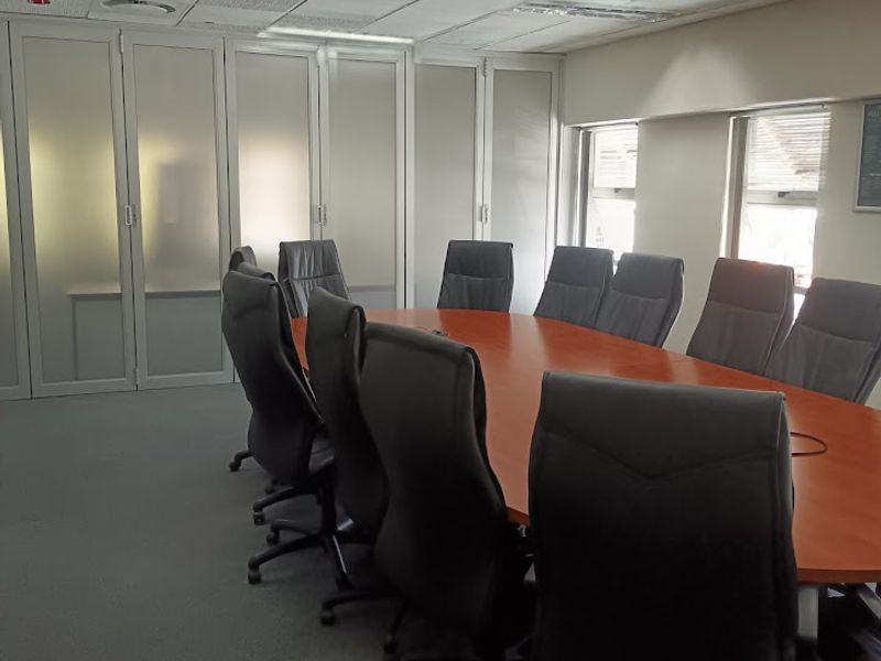 A professional office boardroom featuring a large conference table, carpeted flooring, suspended ceiling with recessed lighting, and frosted glass partition walls.