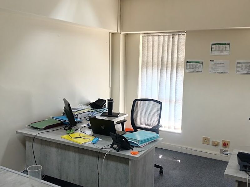A functional office space featuring a suspended ceiling, recessed lighting, vertical blinds, and carpet flooring, providing a practical work environment.