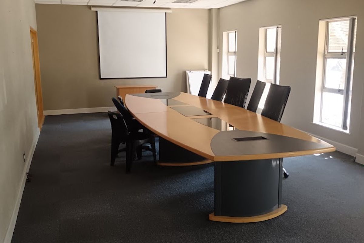 A functional office boardroom featuring a large conference table, suspended ceiling with recessed lighting, and a wall-mounted projector screen.