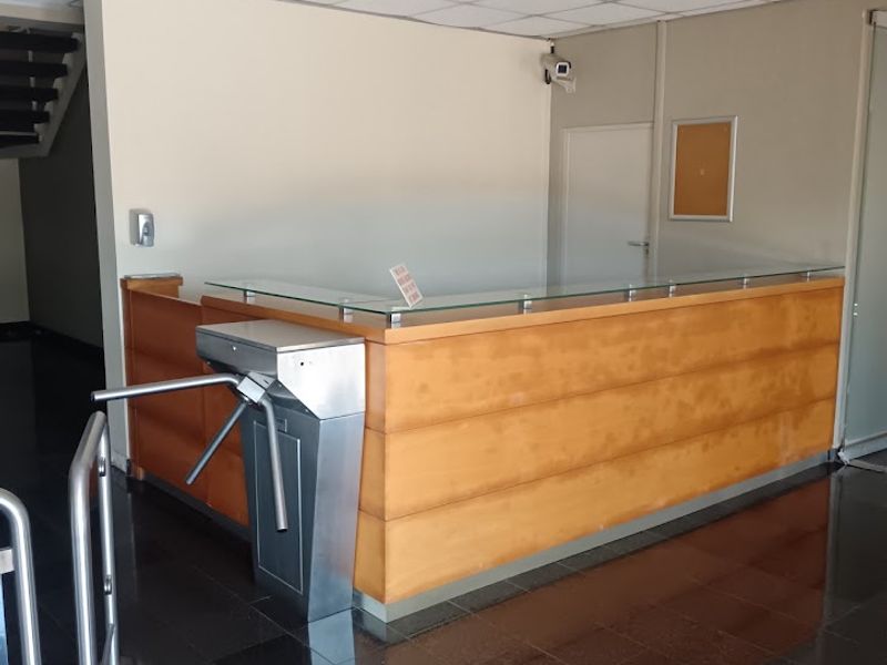 Professional office building entrance featuring a built-in reception desk, security turnstile, and polished tiled flooring in a clean, functional lobby space.