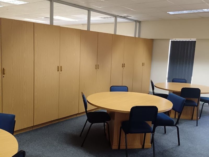 A functional office space featuring built-in storage cabinetry, suspended ceiling tiles, recessed lighting, and glass partition walls.