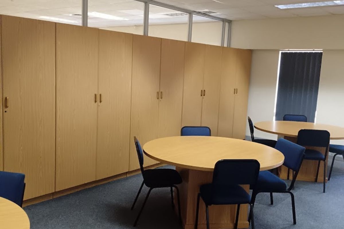 A functional office space featuring built-in storage cabinetry, suspended ceiling tiles, recessed lighting, and glass partition walls.