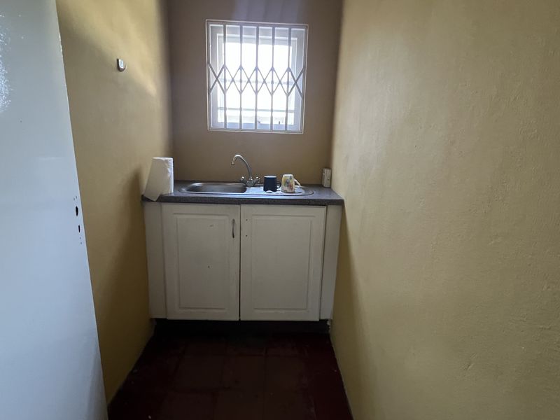A compact scullery area featuring a built-in sink, base cabinetry, and a window with security bars.
