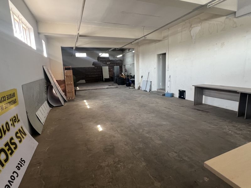 An expansive, industrial-style utility or warehouse space featuring exposed beams, concrete flooring, and high-level windows, requiring cosmetic refurbishment.