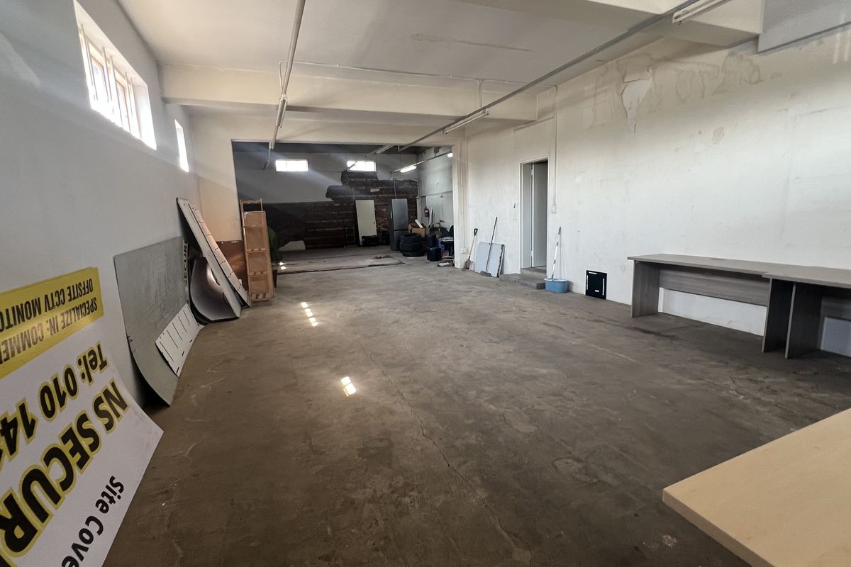 An expansive, industrial-style utility or warehouse space featuring exposed beams, concrete flooring, and high-level windows, requiring cosmetic refurbishment.