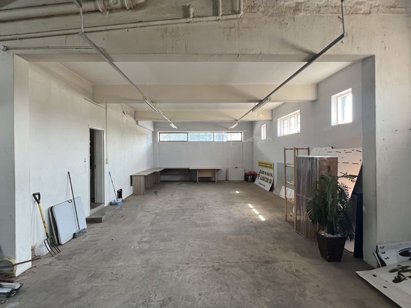 An expansive, open-plan utility or storage space featuring exposed ceiling infrastructure, concrete flooring, and a built-in desk area, suitable for various commercial uses.