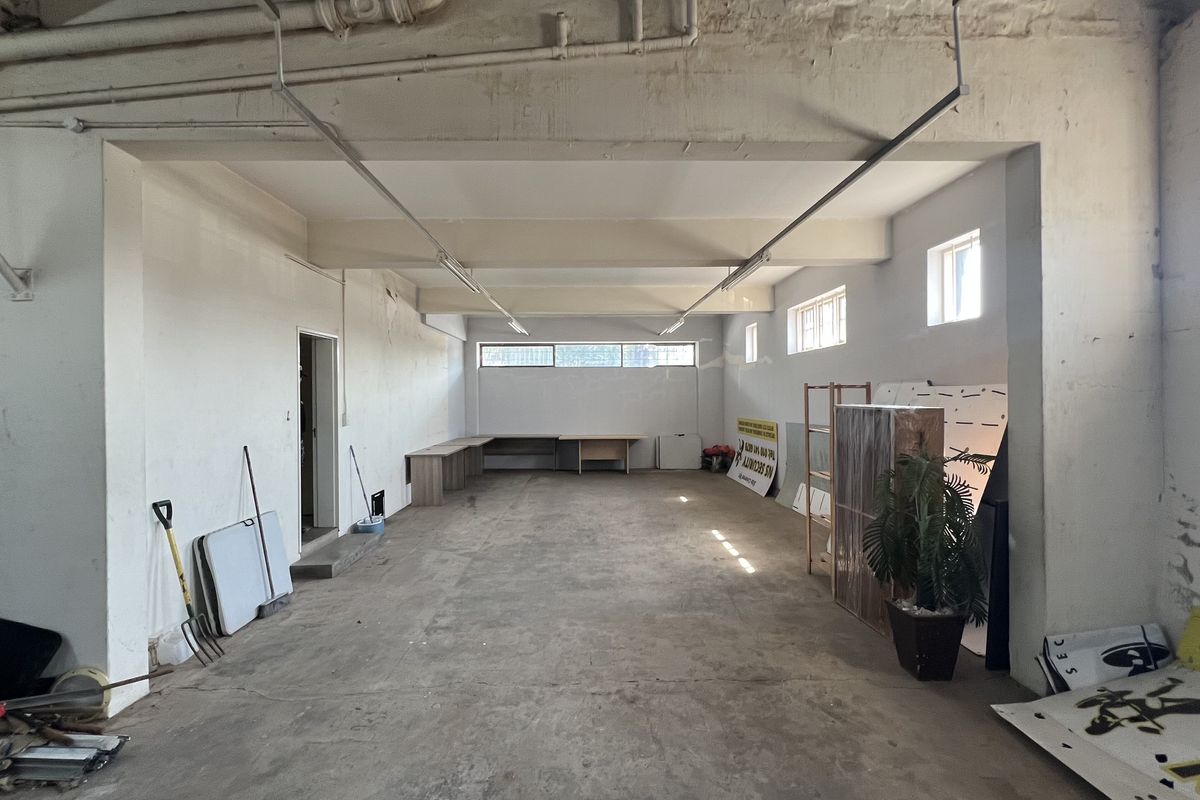 An expansive, open-plan utility or storage space featuring exposed ceiling infrastructure, concrete flooring, and a built-in desk area, suitable for various commercial uses.