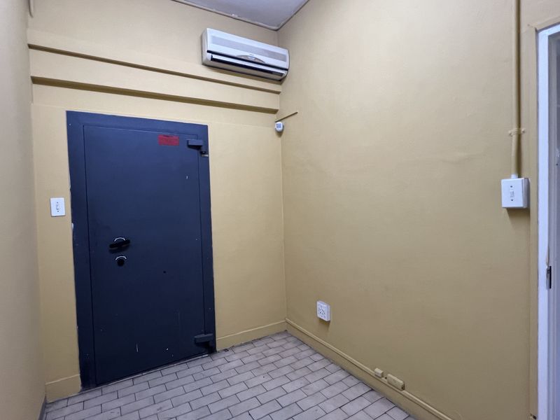 A functional utility room featuring a heavy-duty security door, wall-mounted air conditioning unit, and tiled flooring, suitable for secure storage or office use.