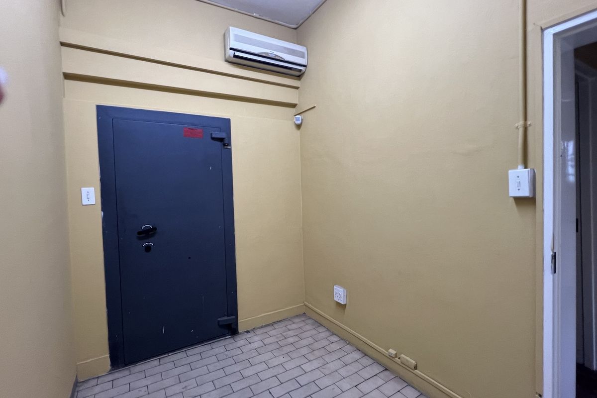 A functional utility room featuring a heavy-duty security door, wall-mounted air conditioning unit, and tiled flooring, suitable for secure storage or office use.