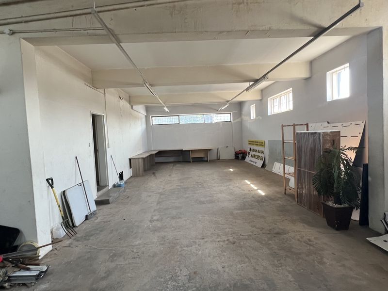 A spacious, open-plan commercial office area featuring exposed ceiling beams, concrete flooring, and built-in desk space, suitable for various business configurations.