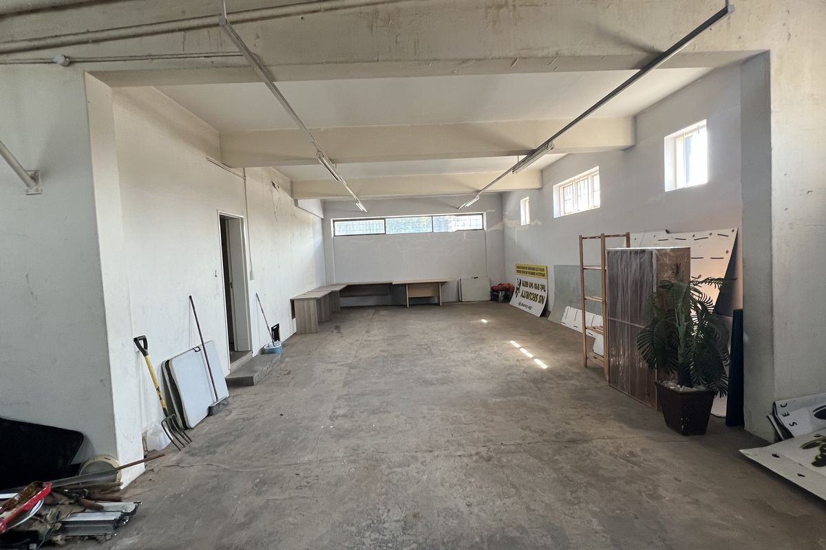 A spacious, open-plan commercial office area featuring exposed ceiling beams, concrete flooring, and built-in desk space, suitable for various business configurations.