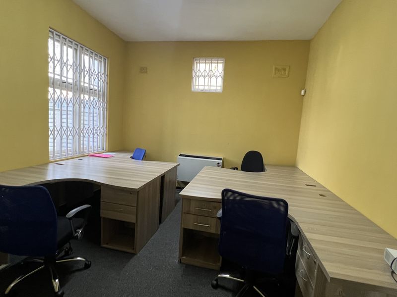 A functional office space featuring built-in desks, security bars on windows, and neutral carpeting, suitable for a professional work environment.