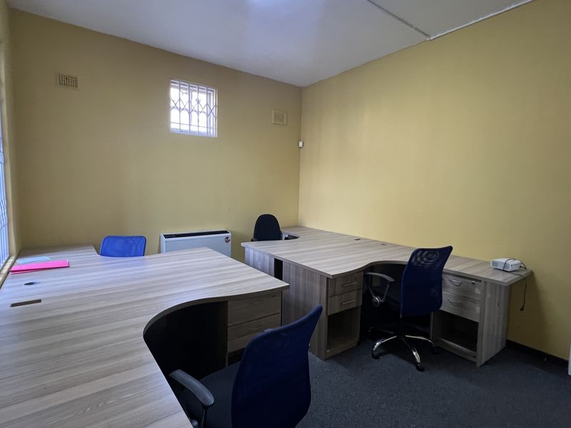 A functional commercial office space featuring built-in desks, carpeted flooring, and security bars on the windows.