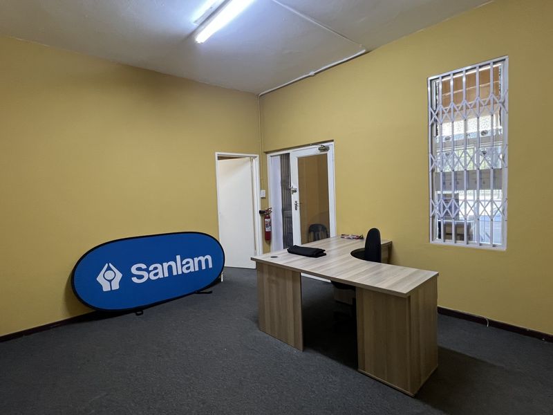 A functional office space featuring yellow walls, carpeted flooring, and a security gate on the window, suitable for a professional commercial workspace.