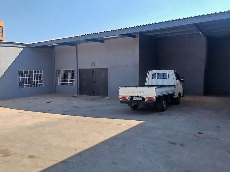 Industrial unit exterior featuring a concrete hardstand, covered loading area, roller shutter door, and secure access point.