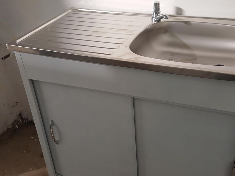 A basic utility area featuring a stainless steel sink unit with a base cabinet, set against an unfinished wall.