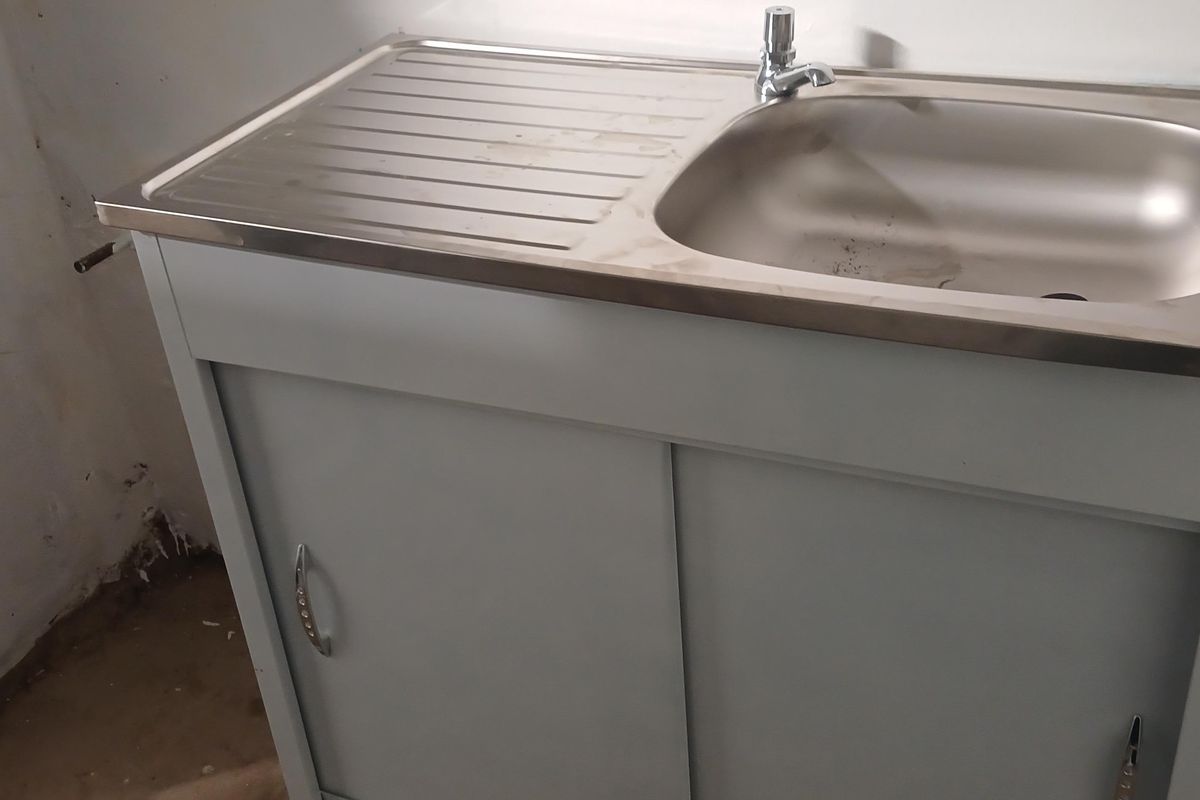 A basic utility area featuring a stainless steel sink unit with a base cabinet, set against an unfinished wall.