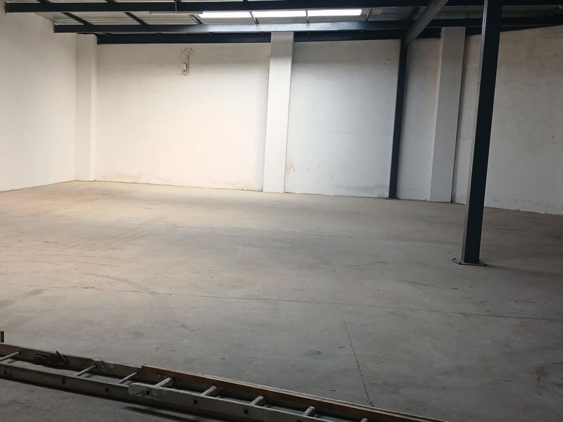 Spacious industrial utility area featuring exposed steel structural beams, concrete flooring, and natural light from a ceiling skylight.